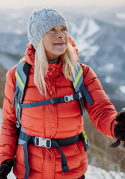 a woman in her 60s wearing a red jacket hiking a snow capped mountain top